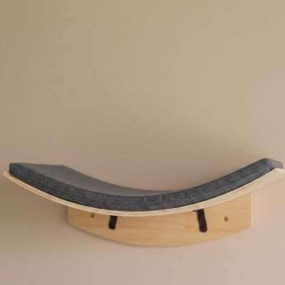 hamac pour chat fixé sur un mur beige en forme circulaire avec un petit coussin gris dessus