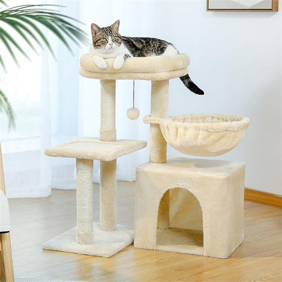 petit arbre a chat de couleur beige avec un chat coucher sur le coussin du haut il a une boule pour le jeu, un hamac et une petite niche